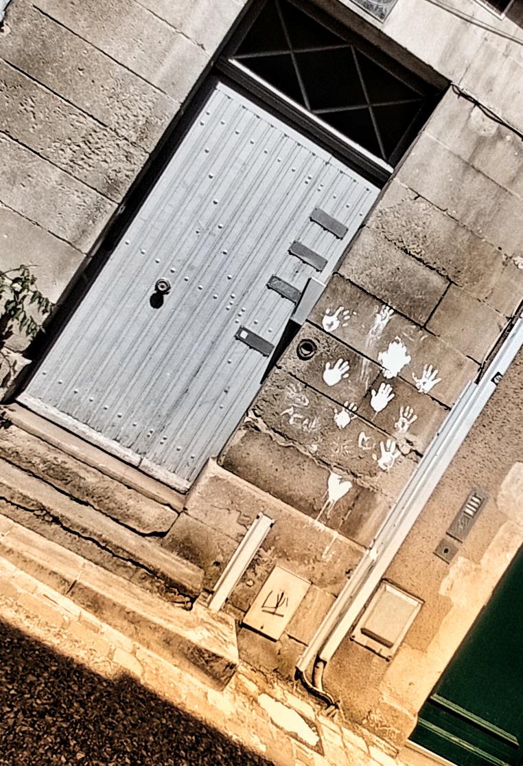 Une porte donnant sur une rue avec juste à côté des mains blanches dessinées sur le mur et plus loin le texte ACAB